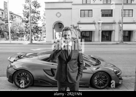 Selbstbewusster Händler spricht auf dem Smartphone neben dem Auto Stockfoto