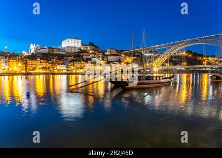 Blick über die traditionellen Rabelo-Boote am Douro-Ufer in Vila Nova de Gaia zur Altstadt von Porto und zur Brücke Dom Luís I in der Dämmerung, Vila Stockfoto