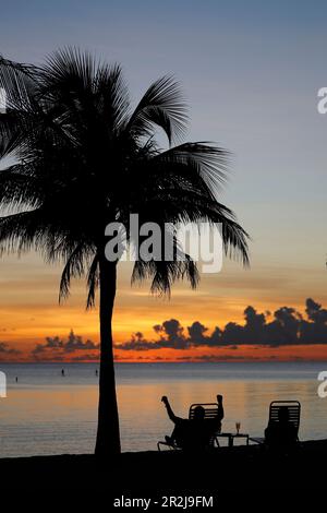 Rentner sitzt auf einem Stuhl bei Sonnenuntergang, tropischer Strand und Paradies Natur, Kaimaninseln, Karibik, Mittelamerika Stockfoto