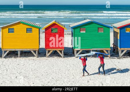 Lächelnde Surfer an Strandhütten und Hütten am Muizenberg Beach, Surfplatz in der Nähe von Kapstadt, Südafrika. Stockfoto