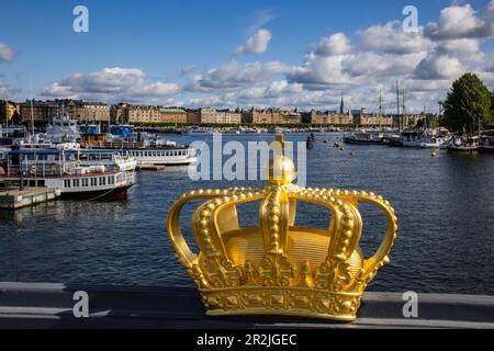 Goldene Krone auf der Skeppsholmen-Brücke mit Booten im Hafen dahinter, Stockholm, Schweden, Europa Stockfoto