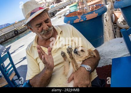 Ein älterer Grieche, der seinen Hündchen im Lombranos Taverna Restaurant neben dem Pier, Fira, Santorin, Südosteuropa, Griechenland, Europa Stockfoto
