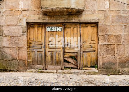 Verrottete Holzdoppeltüren in einer heruntergekommenen Garage an der Fassade eines Steinhauses, Lamego, Portugal Stockfoto