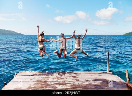 Wasser, der Rücken von Leuten, die von einem Pier springen, Hände halten und zusammen in den Ozean springen, in blauem Himmel. Sommerurlaub oder Urlaub, Freiheit oder Reisen Stockfoto