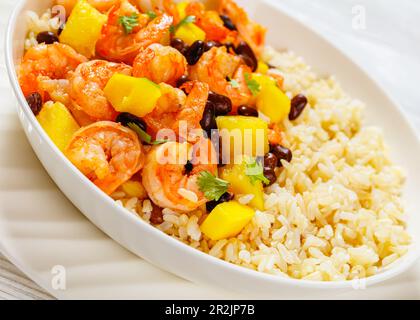 Nahaufnahme von gegrillten Garnelen aus der Karibik mit schwarzen Bohnen, Mango-Ananassalsa serviert mit braunem Reis in einer weißen Schüssel Stockfoto