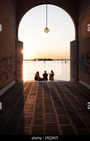 Personen, die bei Sonnenuntergang auf einer Treppe an einem Torbogen sitzen, Cannaregio, Venedig, Venedig, Venetien, Italien, Europa Stockfoto
