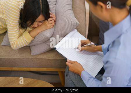Depressive Patientinnen, die auf der Couch liegen und einer Sitzungstherapie durch einen Psychologen zuhören. Stockfoto