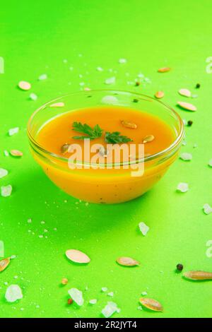 Herbstsuppe mit vegetarischem Kürbis und Karottencreme vor einer lebhaften smaragdgrünen Kulisse Stockfoto