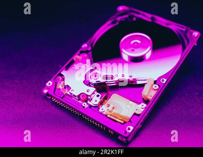 Eine offene Festplatte eines Computers oder Laptops, die zerlegt wurde, liegt auf einer violetten Oberfläche. Computer-Hardware und -Zubehör. Festplattenspeicher. Stockfoto