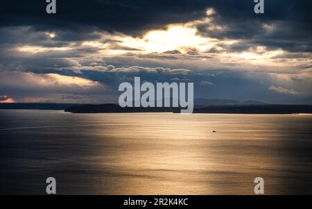 Dramatisches Sonnenlicht durch den wolkigen Himmel über der Meeresoberfläche im Hintergrund der Inseln, Seattle, USA. Stockfoto