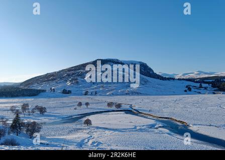 Der Fluss Dee fließt durch das schneebedeckte Tal über der Stadt Braemar, mit den Felsen von Creag Bhalg in der Ferne. Stockfoto