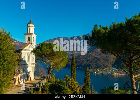 Die Kirche der Heiligen Fedele und Simone und der Luganersee mit dem Berg an einem sonnigen Tag in Vico Morcote, Tessin in der Schweiz. Stockfoto