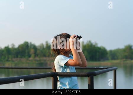 Ein kleines Mädchen, das durch ein Fernglas auf Vögel im Reservoir schaut. Entdeckungs- und Abenteuerkonzept. Vogelbeobachtung Stockfoto