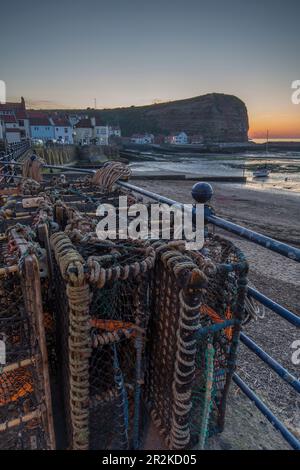 Abendansicht der kleinen Hafenstadt Staithes, Yorkshire, England, Großbritannien. Im Vordergrund Hummerkäfige auf Geländern. Stockfoto