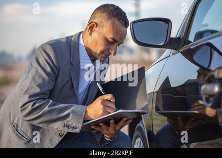 Versicherungsagent, der ein Auto mit einem Kratzer inspiziert und Notizen macht. Stockfoto