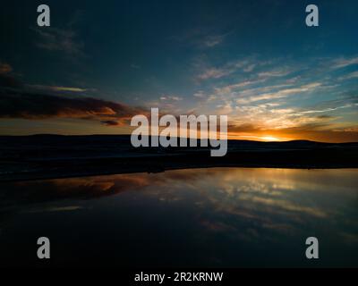 Ein atemberaubender Panoramablick auf Malham Tarn bei Sonnenuntergang, der den lebendigen Himmel und die Kalksteinklippen in seinem ruhigen Wasser reflektiert. Stockfoto