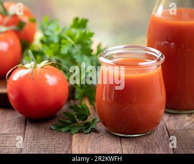 Tomatensaft in Glas und Karaffe mit frischen Tomaten und Petersilie auf einem Holztisch Stockfoto