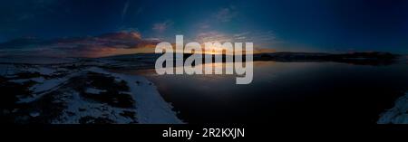 Ein atemberaubender Panoramablick auf Malham Tarn bei Sonnenuntergang, der den lebendigen Himmel und die Kalksteinklippen in seinem ruhigen Wasser reflektiert. Stockfoto