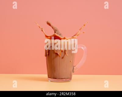 Ein Spritzer Schokoladenmilch aus einem Glas auf pinkfarbenem Hintergrund. Kakao in einem Glas. Ein Spritzer Kakao. Stockfoto