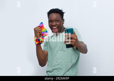 Junger afrikanischer Mann, der jubelt, während er sein Handy hält Stockfoto