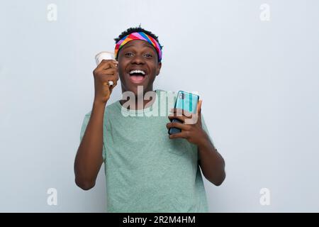 Ein glücklicher junger afrikaner, der Bargeld in der Hand hat und sein Handy benutzt Stockfoto