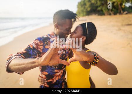 Zwei Liebhaber am Strand machen mit ihren Händen Herzen und haben einen leidenschaftlichen Moment Stockfoto