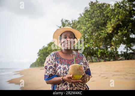 Porträt einer Afrikanerin am Strand, die ihren Urlaub genießt und Kokosmilch trinkt. Stockfoto