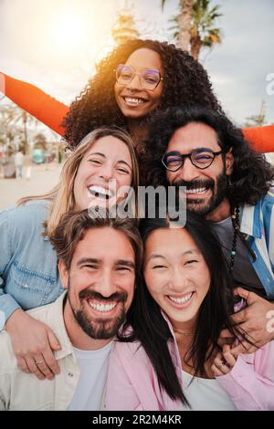 Vertikales Porträt einer Gruppe von Freunden, die zusammen lachen und in die Kamera schauen. Fünf junge, multiethnische Menschen, die lächeln und Spaß haben. Freudige Teamkollegen, die gemeinsam feiern und eine Beziehung aufbauen. Hochwertiges Foto Stockfoto