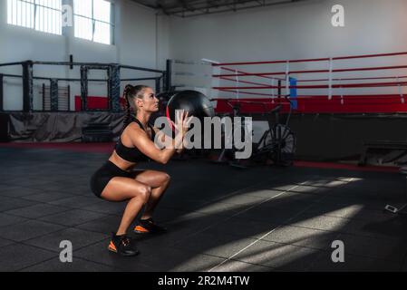 Junge, muskulär schwitzende Fitnessfrau oder Mädchen, die im Fitnessstudio mit dem Wandball trainiert. Konzentrierter weiblicher Wurfmittelball zur Ausdaueranstrengung Stockfoto