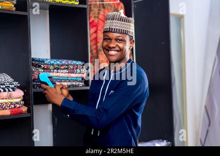 afrikanischer Mann, der auf einem Modemarkt verkauft, mit einem Point-on-Sale-Automaten und lächelnd. Zahlungsart, bargeldlose Transaktion Stockfoto