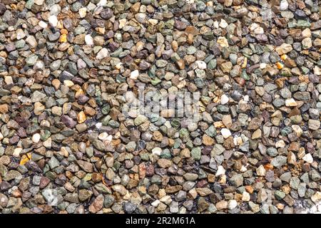 Nasse, farbenfrohe Straßenoberfläche aus zerkleinertem Granit und Kieselsteinen Stockfoto