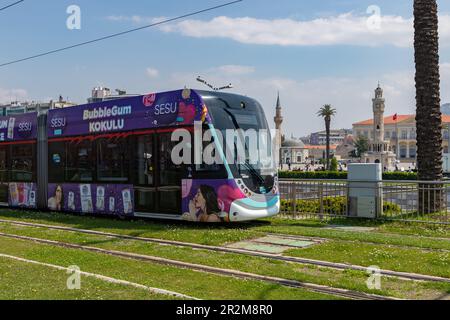 Ein Bild einer Straßenbahn in Izmir, mit dem Uhrturm von Izmir und der Konak-Moschee hinten. Stockfoto