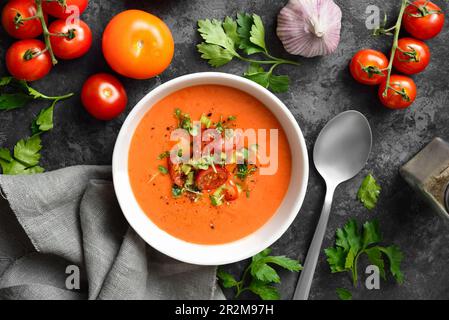 Gazpacho-Suppe und Zutaten auf dunklem Steinhintergrund. Kalte Tomatensuppe. Gesundes Lebensmittelkonzept. Draufsicht, flach liegend Stockfoto