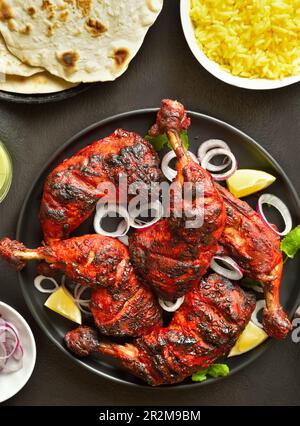 Tandoori-Hühnchen im indischen Stil auf dem Teller mit dunklem Steinhintergrund. Hähnchenschenkel mariniert in Joghurt und Gewürzen. Draufsicht, flach liegend Stockfoto