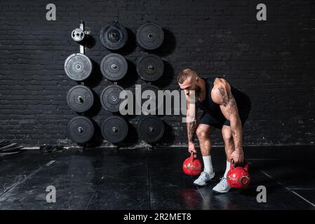 Junger aktiver, starker, schweißtreibender, fokussierter Mann mit großen Muskeln hält schwere Kugelhantel mit Heckengewichten für ein anstrengendes Cross-FIT-Training Stockfoto
