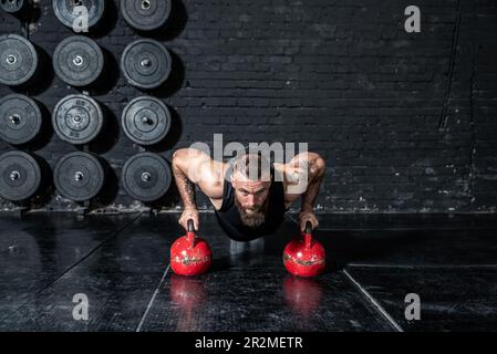 Junger aktiver, starker, schweißtreibender, fokussierter Mann mit großen Muskeln hält schwere Kugelhantel mit Heckengewichten für ein anstrengendes Cross-FIT-Training Stockfoto