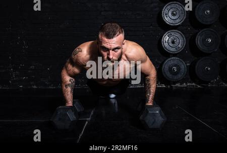 Junger aktiver, starker, schweißtreibender, fokussierter Mann mit großen Muskeln hält schwere Kugelhantel mit Heckengewichten für ein anstrengendes Cross-FIT-Training Stockfoto