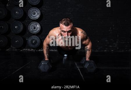 Junger aktiver, starker, schweißtreibender, fokussierter Mann mit großen Muskeln hält schwere Kugelhantel mit Heckengewichten für ein anstrengendes Cross-FIT-Training Stockfoto