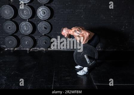 Junger aktiver, starker, schweißtreibender, fokussierter Mann mit großen Muskeln hält schwere Kugelhantel mit Heckengewichten für ein anstrengendes Cross-FIT-Training Stockfoto