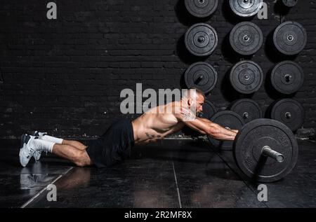 Junger aktiver, starker, schweißtreibender, fokussierter Mann mit großen Muskeln hält schwere Kugelhantel mit Heckengewichten für ein anstrengendes Cross-FIT-Training Stockfoto
