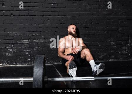 Junger aktiver, starker, schweißtreibender, fokussierter Mann mit großen Muskeln hält schwere Kugelhantel mit Heckengewichten für ein anstrengendes Cross-FIT-Training Stockfoto