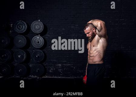 Junger aktiver, starker, schweißtreibender, fokussierter Mann mit großen Muskeln hält schwere Kugelhantel mit Heckengewichten für ein anstrengendes Cross-FIT-Training Stockfoto