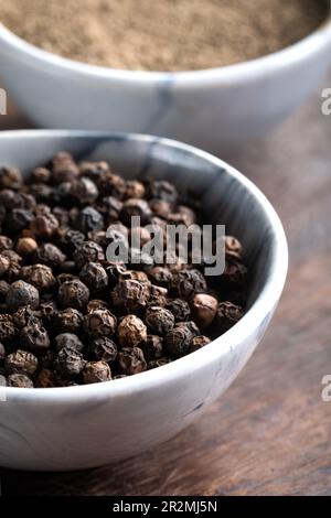 Schwarze Pfefferkörner (Schwarzer Pfeffer) in einer Schüssel auf Holzhintergrund. Stockfoto