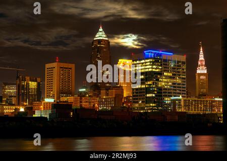 In der Innenstadt von Cleveland, Ohio, vom Westufer des Cuyahoga, wo der Vollmond hinter den Wolken aufgeht Stockfoto