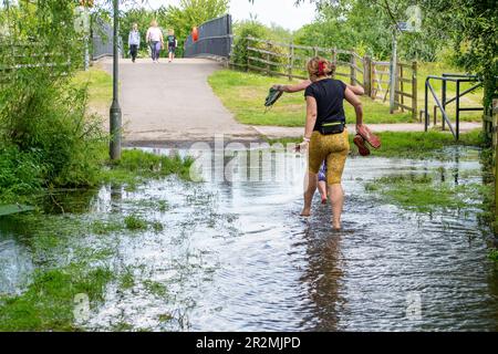 Eton Wick, Windsor, Großbritannien. 20. Mai 23. Jogger ziehen ihre Sportschuhe auf einem öffentlichen, überfluteten Fußweg aus. Der Roundmoor Graben Bach in Eton Wick ist wieder überflutet und bietet Wanderern Zugang zum Jubilee River Fußweg von Eton Wick, der nur mit dem Fahrrad oder in wellington Stiefeln zugänglich ist. Die nahegelegene Brücke über den Jubilee River wird regelmäßig von Einheimischen genutzt, die nach Asda in Cippenham gehen, um ihre Lebensmittel einzukaufen. Der Roundmoor-Graben ist bereits übergelaufen, als das Wasser der Themse angeblich überschüssiges Wasser aus den Kläranlagen der Themse in den Fluss gepumpt hat. Kredit: Maureen MCL Stockfoto