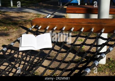 Komfortable NetzHängematte mit offenem Buch im Freien an sonnigen Tagen Stockfoto