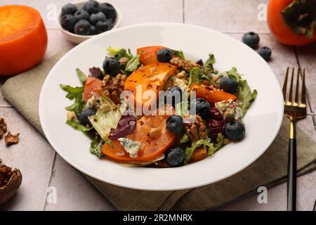 Köstlicher Persimonsalat und Gabel auf gefliester Oberfläche Stockfoto