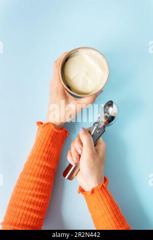 Das Mädchen hält cremiges Eis in der Hand in einem handgefertigten Eimer. Eislöffel. Blauer Hintergrund, Kopierraum Stockfoto