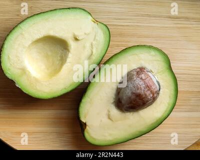 Zwei Scheiben Avocado auf Holzhintergrund. Gesundes Essen. Zwei Hälften Avocado. Eine Scheibe mit Kern. Draufsicht. Speicherplatz kopieren. Selektiver Fokus. Stockfoto