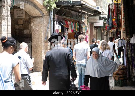Eine palästinensische Frau geht in der Altstadt Jerusalems an einem ultra-orthodoxen jüdischen Mann vorbei, bevor die israelische Flagge marschiert. Zehntausende nahmen an den jährlichen Feierlichkeiten zum Jerusalem-Tag Teil, die die Vereinigung der Stadt im Israel-Arabischen Krieg von 1967 markieren. Der marsch ging durch das Damescus-Tor und die Altstadt. Stockfoto